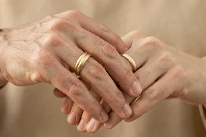 Deux mains adultes enlacées portant des bagues duo homme femme en or sur fond neutre chaleureux